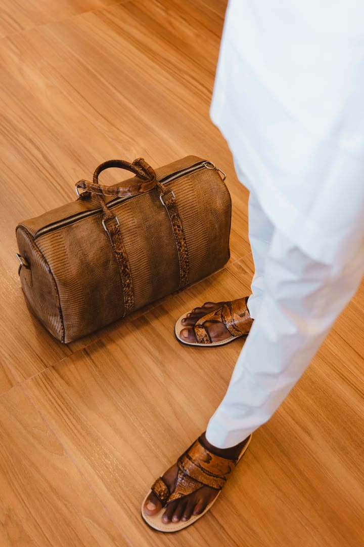 Python-trimmed sandals and duffel on a wooden floor